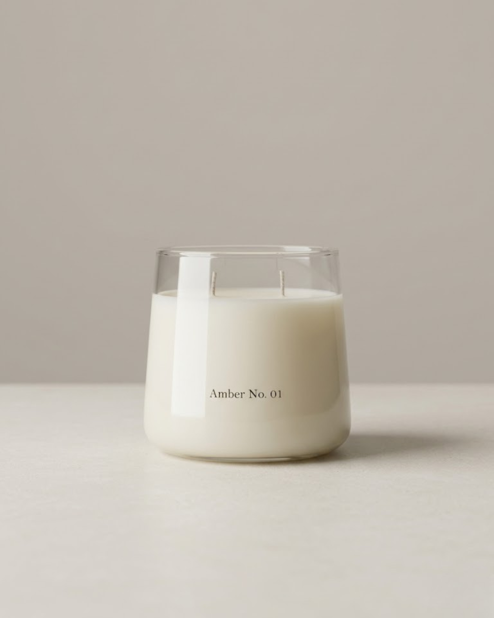 White candle in a glass container labeled 'Amber No. 01' on a neutral background